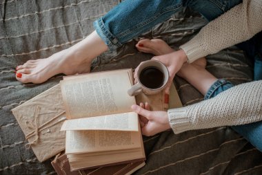 kız bir kitap okuma ve duvarda yatak ayakları kahve içme.