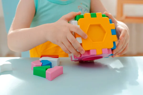 Närbild av barnets händer samla pussel sortera. Kub med inlagda geometriska former och färgade plastblock. — Stockfoto