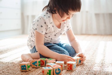 çocuk odada katta harflerle ahşap bloklar ile oynar küçük bir kız evde ya da anaokulunda bir kule inşa ediyor.
