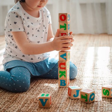 çocuk odada katta harflerle ahşap bloklar ile oynar küçük bir kız evde ya da anaokulunda bir kule inşa ediyor.