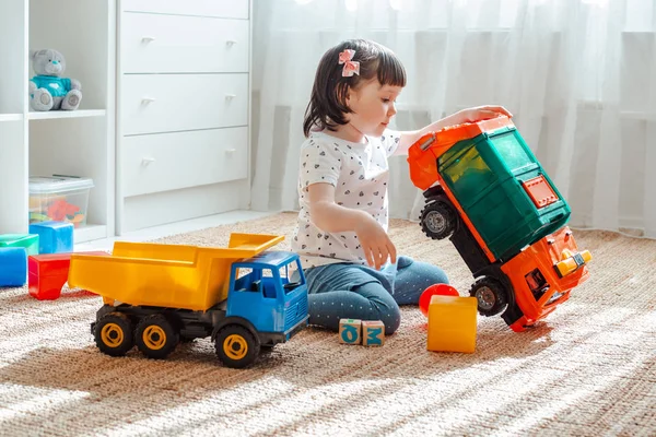 The concept of childhood and people is a happy three year old girl playing with a toy car at home. — Stock Photo, Image