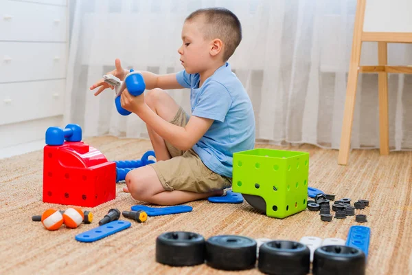 Pequeno menino de 6 anos recolhe o designer de peças grandes e pesadas . — Fotografia de Stock