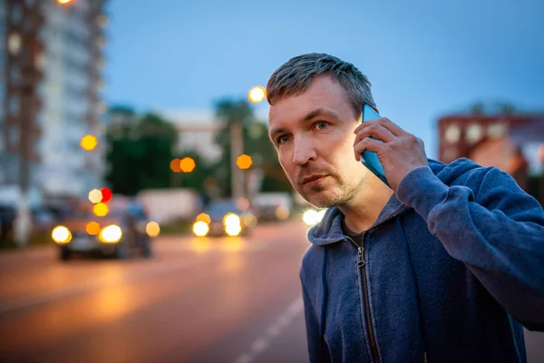 Hipster hombre hablando en un teléfono móvil por la noche en la ciudad en el fondo de las luces bokeh . — Foto de Stock