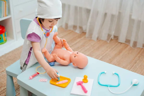 Little girl 3 years old preschooler playing doctor with doll. The child makes an injection toy. — Stock Photo, Image