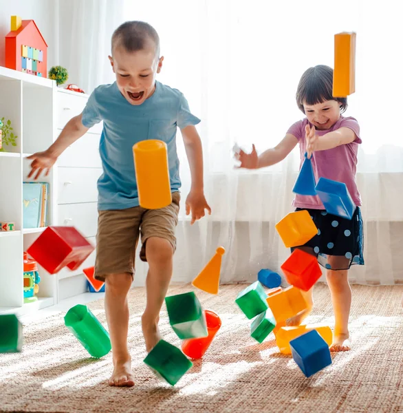 Mały brat i siostra biegać po pokoju rozprzestrzeniania nogi zabawki raznocvetnye bloki plastikovye. — Zdjęcie stockowe