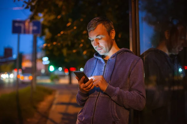 Hipster hombre hablando en un teléfono móvil por la noche en la ciudad en el fondo de las luces bokeh . — Foto de Stock