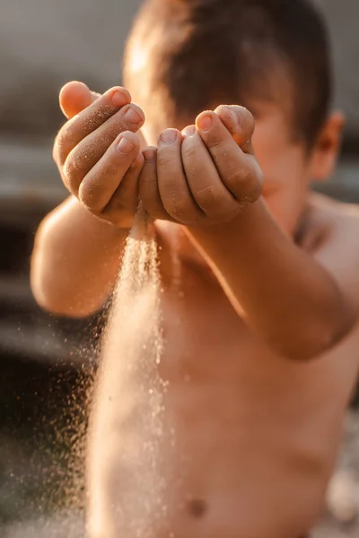 Τα χέρια των παιδιών απελευθερώνουν την άμμο που πέφτει. Άμμος που ρέει μέσα από τα χέρια σας στο ηλιοβασίλεμα του ήλιου. — Φωτογραφία Αρχείου