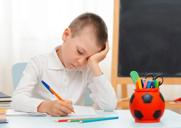 Niño de la escuela sentado en el aula de casa tumbado escritorio lleno de libros material de formación escolar durmiendo perezoso aburrido — Foto de Stock