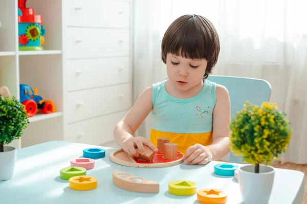 Niña recoge una pirámide de madera sin pintar. Juguetes naturales seguros de madera para niños. — Foto de Stock