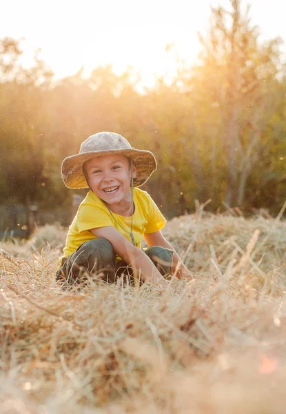 Kleiner Junge, der auf der Höhe eines großen Heuhaufens im Dorf sitzt. das Kind der Bauer. — Stockfoto