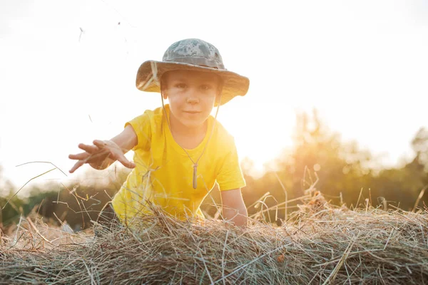 Kleiner Junge, der auf der Höhe eines großen Heuhaufens im Dorf sitzt. das Kind der Bauer. — Stockfoto