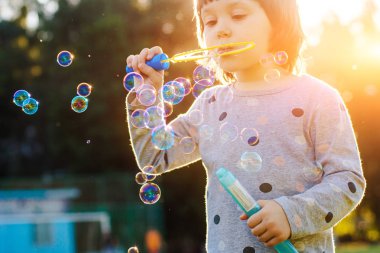 Gün batımı arka plan ile Playground üzerinde kabarcıklar üfleme Çocuklar küçük kız