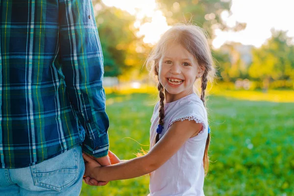 Little girl kid daughter holding her fathers hand in the background of nature at sunset. — Stock Photo, Image