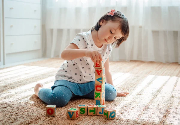 Dziecko gra z drewnianych bloków z literami na podłodze w pokoju mała dziewczynka buduje wieżę w domu lub w przedszkolu. — Zdjęcie stockowe