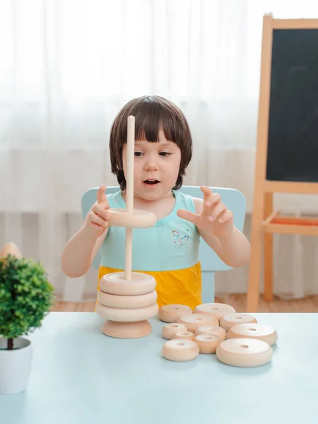 Küçük kız boyanmamış ahşap bir piramit topluyor. Güvenli doğal ahşap çocuk oyuncakları. — Stok fotoğraf