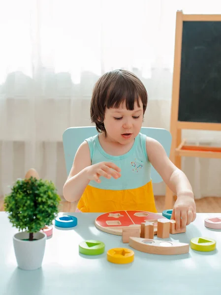 Niña recoge una pirámide de madera sin pintar. Juguetes naturales seguros de madera para niños. —  Fotos de Stock