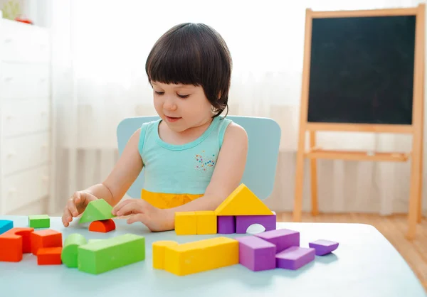 Little girl collects a wooden unpainted pyramid. Safe natural wooden children's toys. — Stock Photo, Image