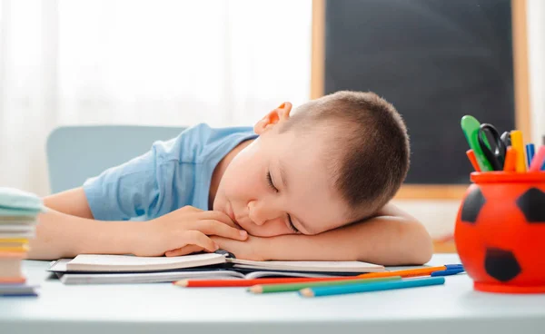 Niño de la escuela sentado en el aula de casa tumbado escritorio lleno de libros material de formación escolar durmiendo perezoso aburrido — Foto de Stock