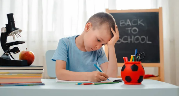 Niño de la escuela sentado en el aula de casa tumbado escritorio lleno de libros material de formación escolar durmiendo perezoso aburrido — Foto de Stock