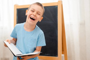 Açık bir not defteri ile okul tebeşir tahtasında duran öğrenci. Okula hazırlık.