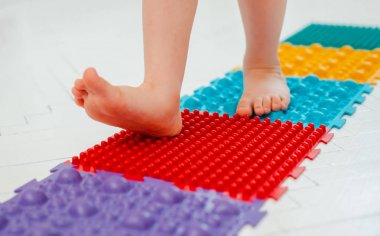 Bebek ayak masajı minderinde yeni yürümeye başlayan çocuk. Ortopedik masaj halısı üzerinde bacak egzersizleri. Düz taban ve halluks valgus önleme