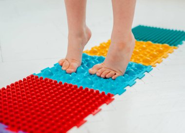 Bebek ayak masajı minderinde yeni yürümeye başlayan çocuk. Ortopedik masaj halısı üzerinde bacak egzersizleri. Düz taban ve halluks valgus önleme