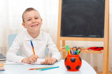 Okullu çocuk sınıfında oturmuş kitap dolu bir masada yatıyor. Uyuyan tembel öğrencileri eğitiyor.