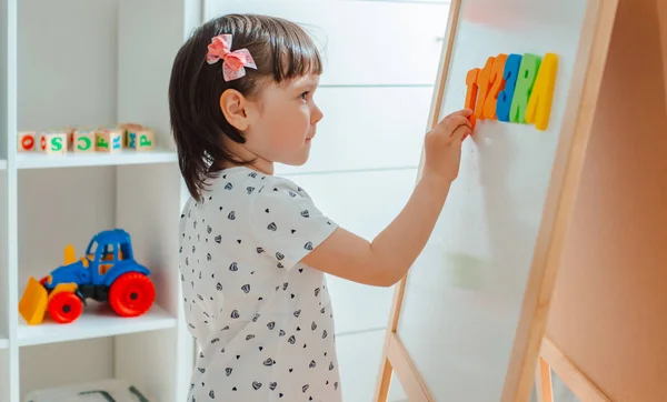 Criança brinca com blocos de madeira com letras no chão na sala uma menina está construindo uma torre em casa ou no jardim de infância . — Fotografia de Stock