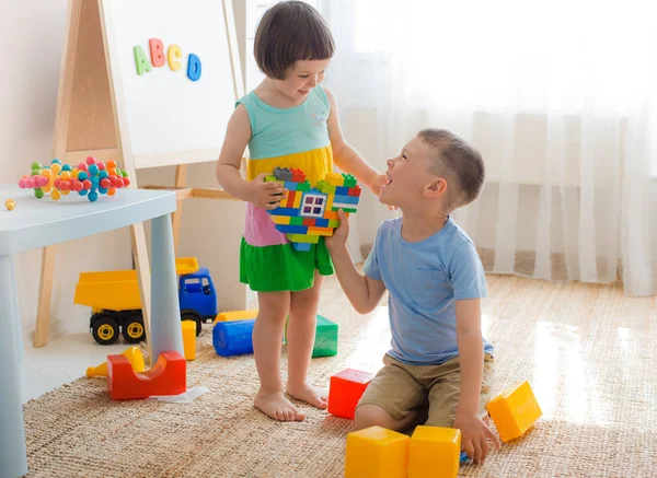 Um menino e uma menina estão segurando um coração feito de blocos de plástico. Irmão e irmã se divertir jogando juntos no quarto. — Fotografia de Stock