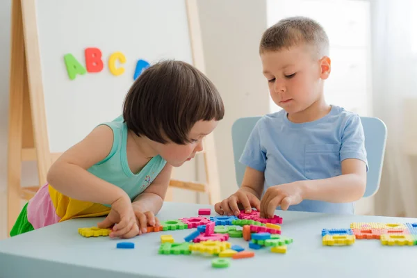 Chłopiec i dziewczyna zbierają miękkie puzzle przy stole. Bawcie się dobrze razem w pokoju.. — Zdjęcie stockowe