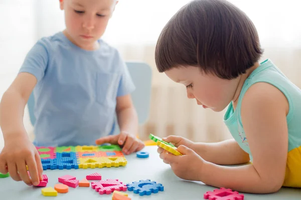 Um menino e uma menina coletam um quebra-cabeça suave na mesa. Irmão e irmã se divertir jogando juntos no quarto. — Fotografia de Stock
