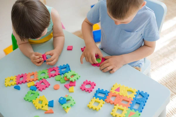 Chłopiec i dziewczyna zbierają miękkie puzzle przy stole. Bawcie się dobrze razem w pokoju.. — Zdjęcie stockowe