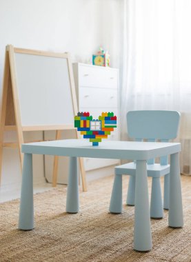 Parlak beyaz bir odanın içi. Oyuncak çocuk masası. Masanın üzerinde kalp şeklinde çok renkli bir tasarımcı var..