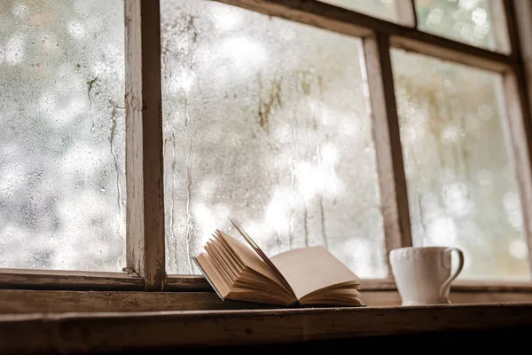 Een witte kop en oude boeken op de achtergrond van een rustiek houten natte ruit — Stockfoto