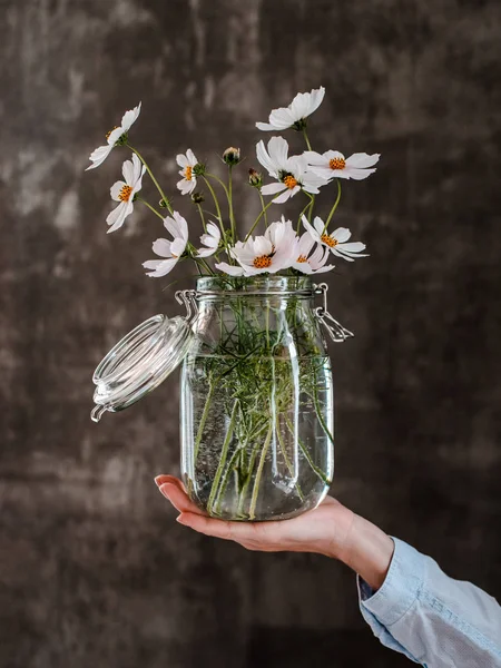 Ramo de flores blancas en un frasco de vidrio en las manos de una florista niña en el fondo de una pared de hormigón. — Foto de Stock