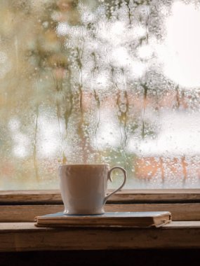 Bir rustik ahşap ıslak pencerenin arka planda beyaz bir Fincan ve eski kitaplar