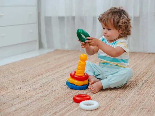 Bebê joga no chão na sala em brinquedos plásticos educativos . — Fotografia de Stock