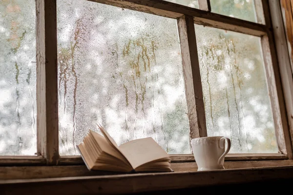 Biała filiżanka i stare książki na tle rustykalnego drewnianego okna mokrego — Zdjęcie stockowe