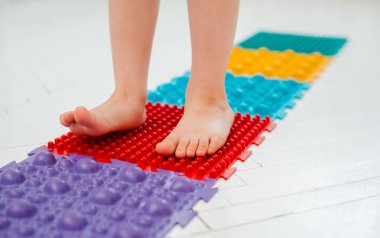 Bebek ayak masajı minderinde yeni yürümeye başlayan çocuk. Ortopedik masaj halısı üzerinde bacak egzersizleri. Düz taban ve halluks valgus önleme