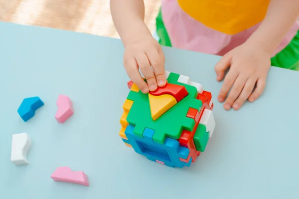 Zbliżenie rąk dziecka zbierać sorter puzzle. Kostka z wstawionymi geometrycznymi kształtami i kolorowymi plastikowymi klockami. — Zdjęcie stockowe