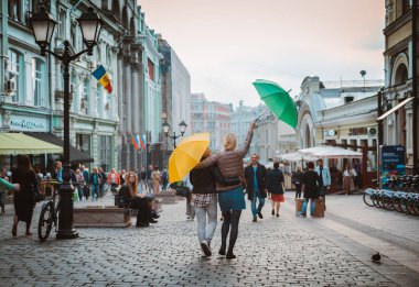 İki arkadaş sonbahar veya bahar mevsiminde şehir merkezinde parlak şemsiyeler altında yürürler. Arkadaşlık konsepti, sezon dışı, seyahat Rusya, Moskova 06 Eylül 2019