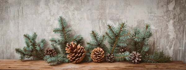 灰色のコンクリート壁に対して暗い木製のボード上のコーンとクリスマスツリーの枝. — ストック写真