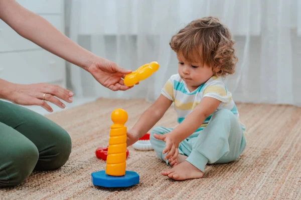 Anne ve çocuk, çocuk odasında yerde oynuyorlar. Anne ve küçük bebek plastik renkli oyuncaklarla oynuyorlar.. — Stok fotoğraf