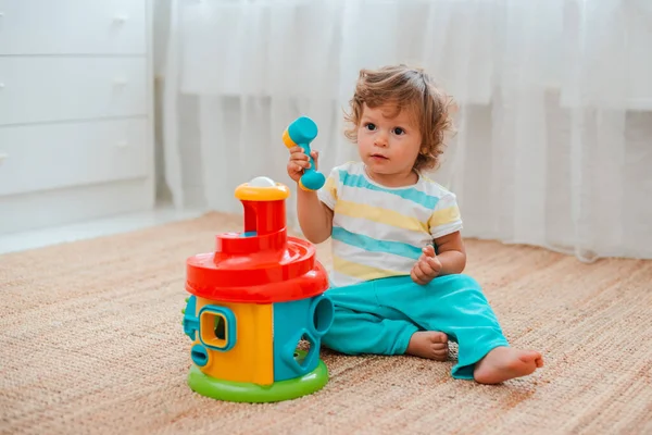 Bebê joga no chão na sala em brinquedos plásticos educativos . — Fotografia de Stock