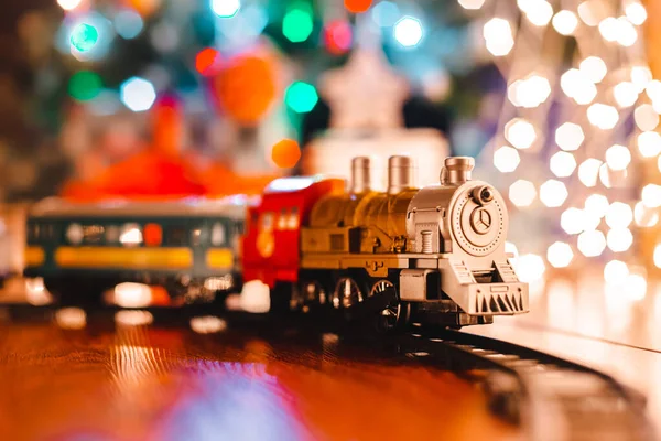 Παιχνίδι vintage ατμομηχανή στο πάτωμα κάτω από ένα διακοσμημένο χριστουγεννιάτικο δέντρο σε φόντο bokeh φώτα γιρλάντα. — Φωτογραφία Αρχείου