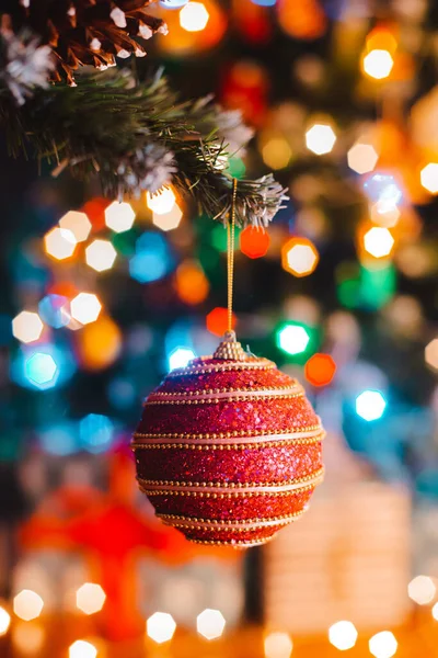 Bola de Natal pendura em um abeto decorado contra o fundo de luzes de bokeh ardentes à noite . — Fotografia de Stock