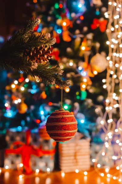 Kerstbal hangt aan een versierde dennenboom tegen de achtergrond van brandende bokeh lichten 's nachts. — Stockfoto