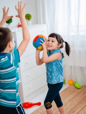 Yerli çocuklar, bir kız ve bir erkek çocuk oyun odasında top oynuyorlar. Bebeklerin etkileşimi, iletişim, karşılıklı oyun, karantina, evdeki kendini izolasyon