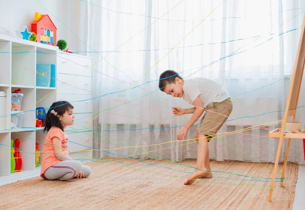 Menina menino irmão, irmãos, friendschild sobe através de uma teia de corda, uma busca obstáculo jogo dentro de casa . — Fotografia de Stock