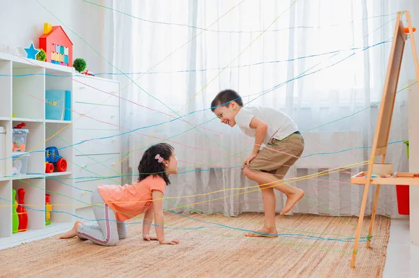 Menina menino irmão, irmãos, friendschild sobe através de uma teia de corda, uma busca obstáculo jogo dentro de casa . — Fotografia de Stock